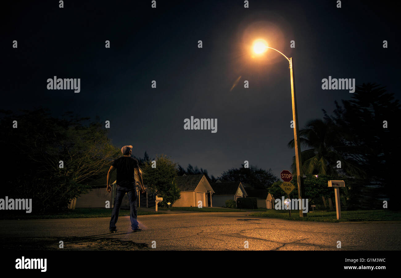 Caucasian man looking up at street light in suburb at night Stock Photo