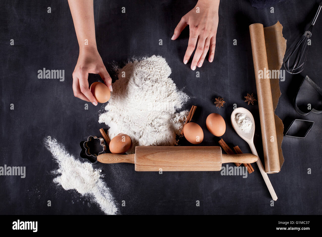 Ingredients like eggs, flour, cinnamon, anise, rolling pin, paper on blackboard Stock Photo