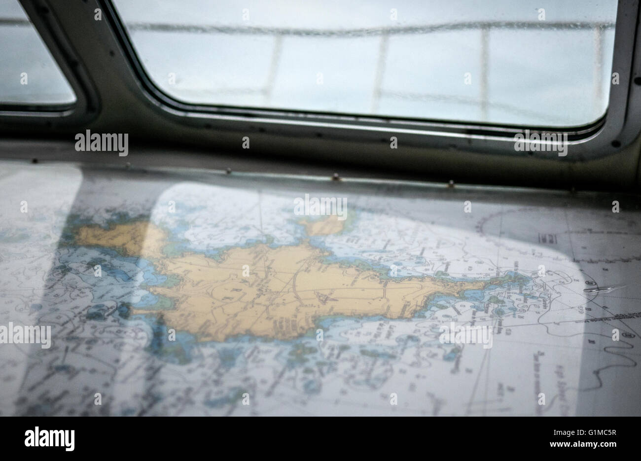 A nautical navigation chart laid out beneath a yacht’s window while sailing at sea. Stock Photo