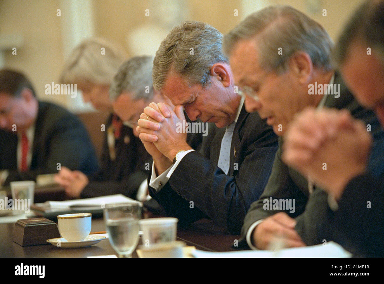U.S President George W. Bush bows his head as Secretary of Defense Donald Rumsfeld, right, says a prayer before the start of a cabinet meeting in the Cabinet Room of the White House September 14, 2001 in Washington, DC. This was the first meeting of the full cabinet following the terror attacks on September 11th. Stock Photo