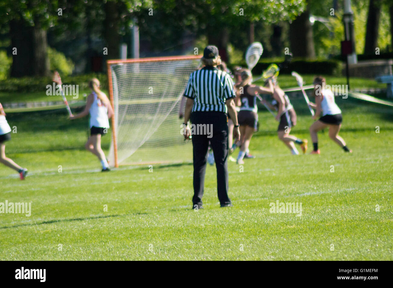 Girls battling at lacrosse on a spring day while the referee stands and watch Stock Photo