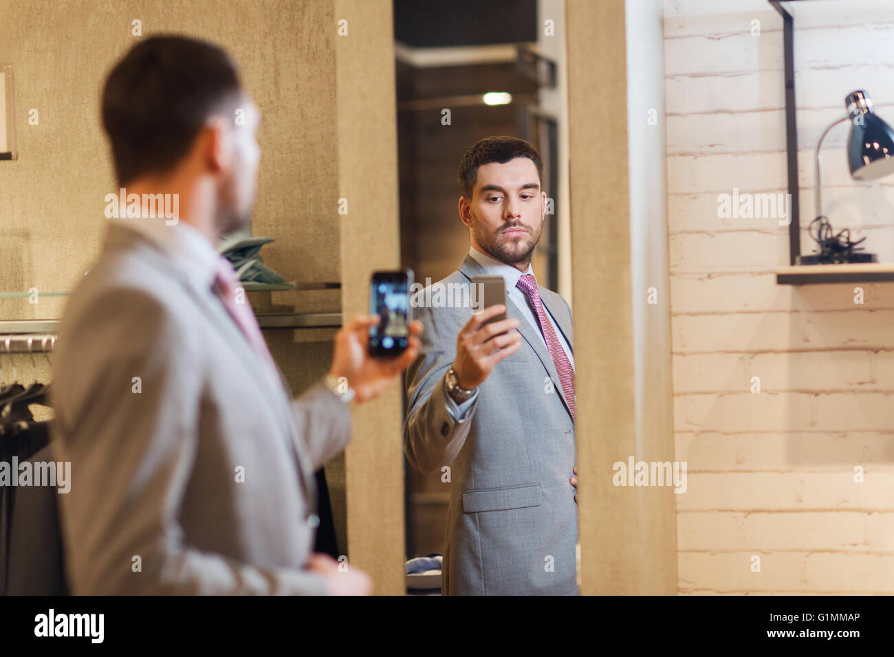 man in suit taking mirror selfie at clothing store Stock Photo