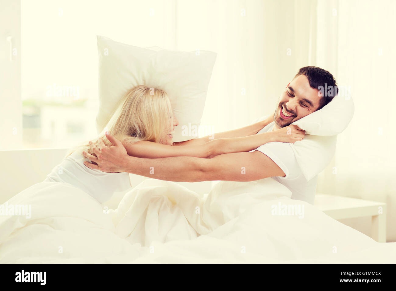 happy couple having pillow fight in bed at home Stock Photo