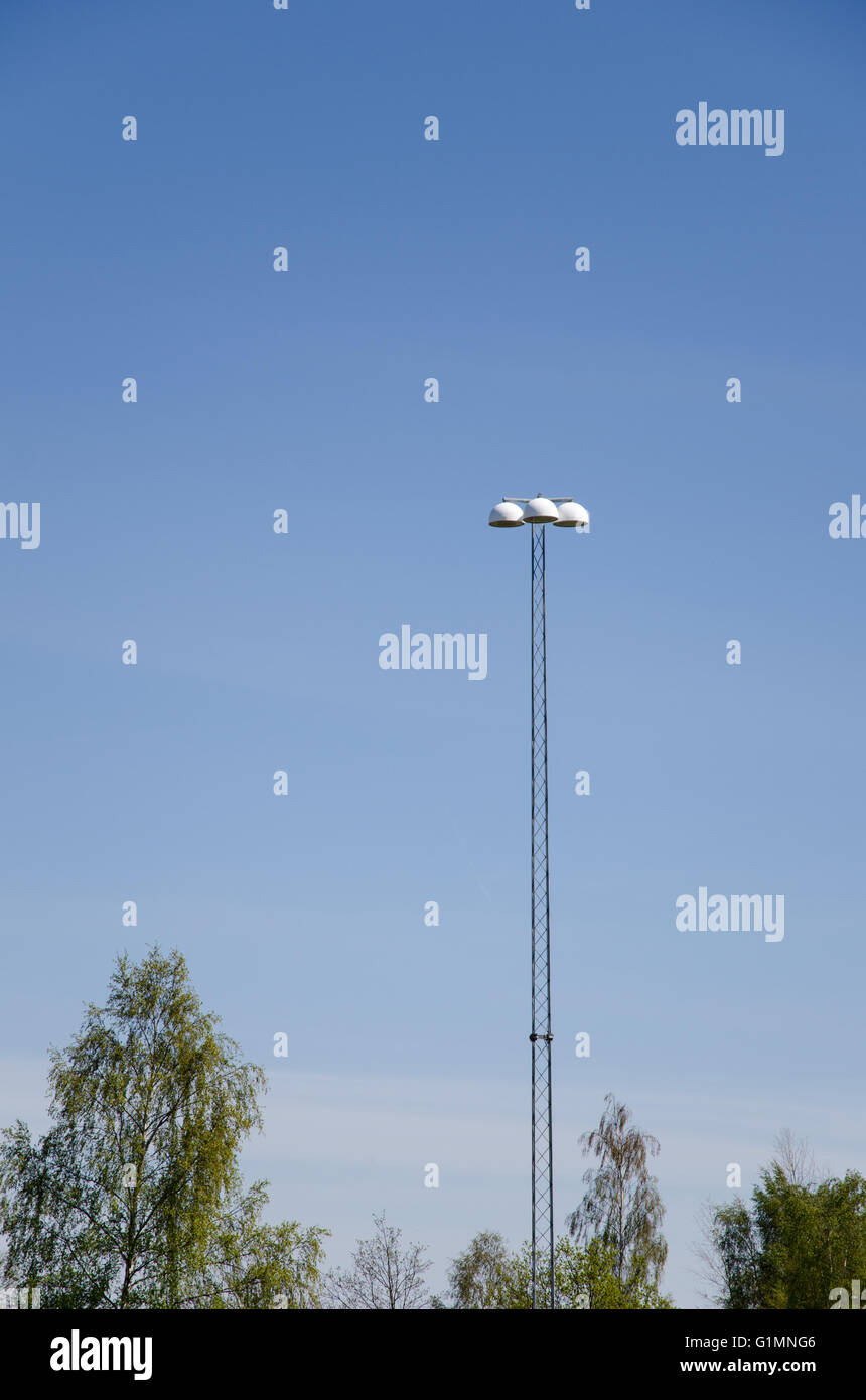 Tall road lighting post with blue sky and tree tops at the bottom of the image Stock Photo