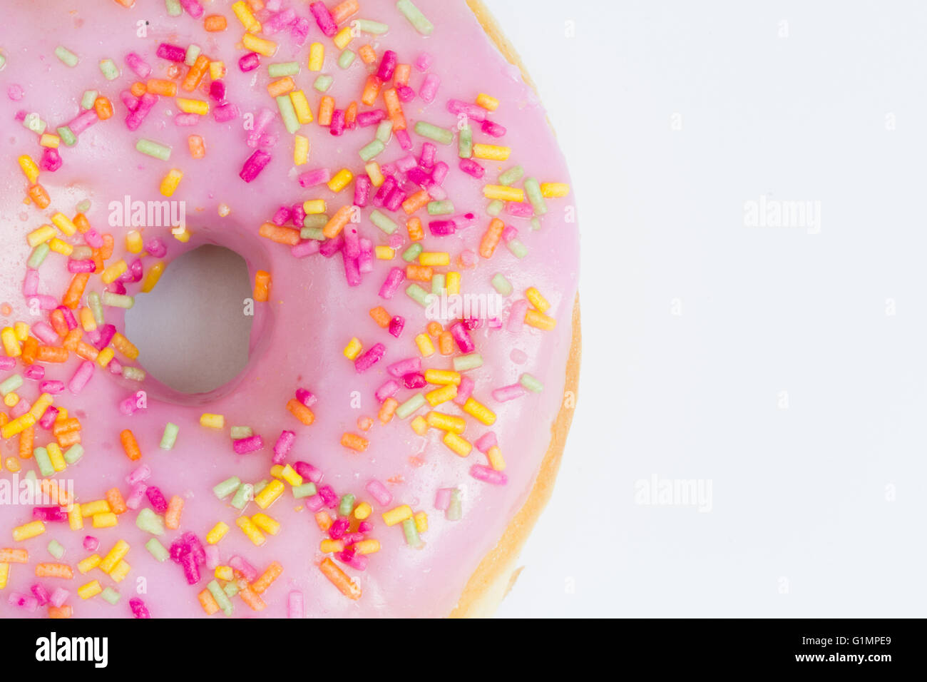 A large donut with pink icing and sprinkles showing its hole on an isolated white background. Stock Photo