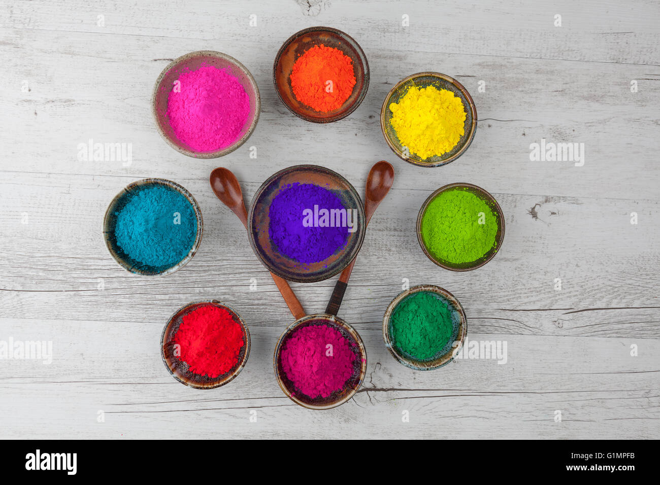 Vibrant colorful Holi powder in cups arranged in circle with two wooden cups. Top view. Stock Photo