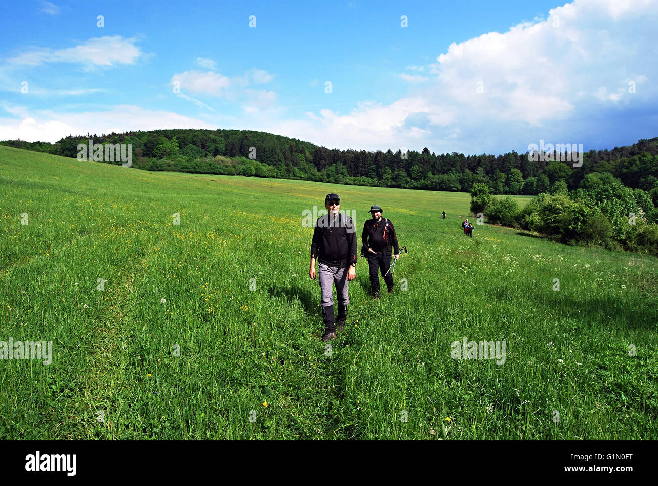 hikers on spring meadow with hills on the background and blue sky with clouds in Strazovske vrchy mountains Stock Photo