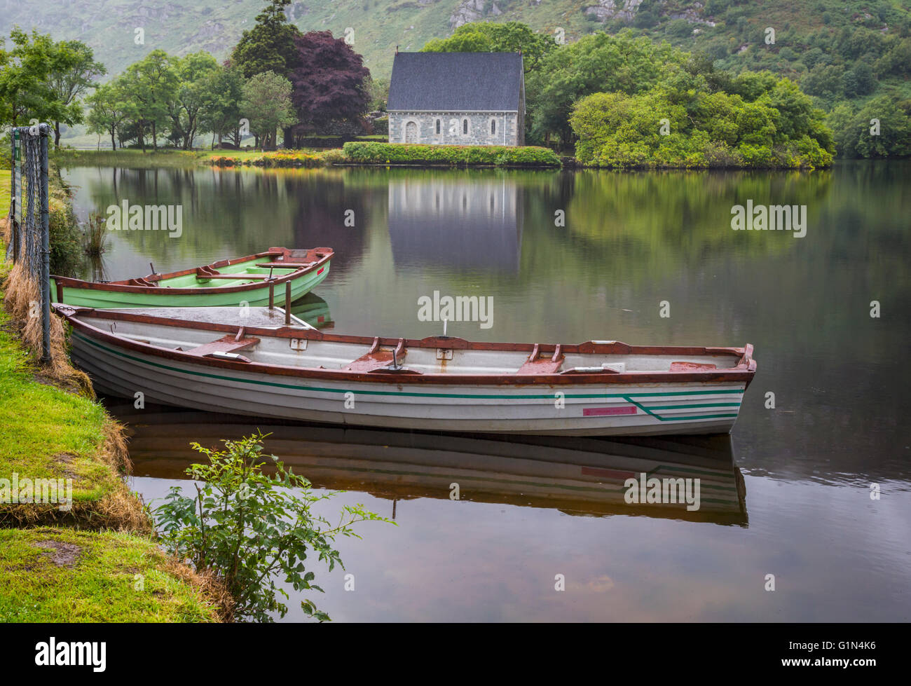 Gougane Barra, County Cork, Republic of Ireland.  Eire.  Looking across rowing boats moored at the lake shore with the Hermitage Stock Photo