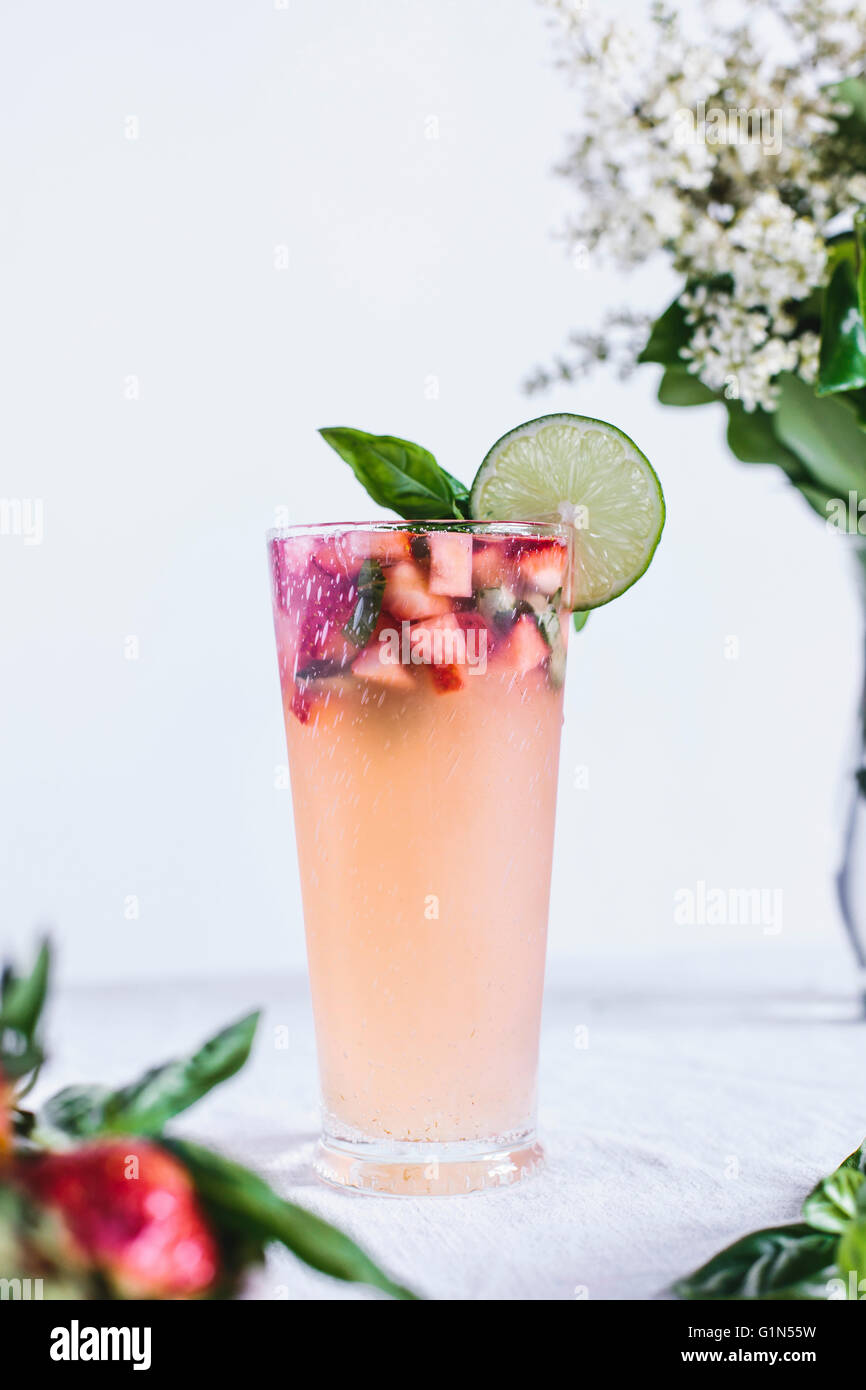 A glass full of Honey Sweetened Limeade with Strawberries and Basil is photographed from the front view. Stock Photo