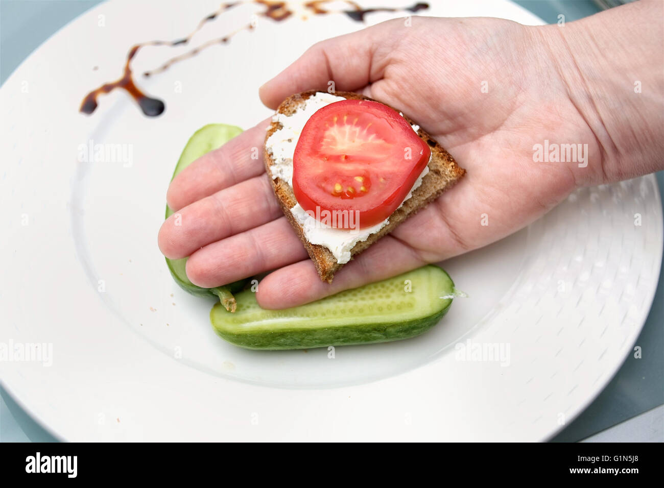 Hand holding a sandwich with spread and tomato, overhead closeup shot Stock Photo