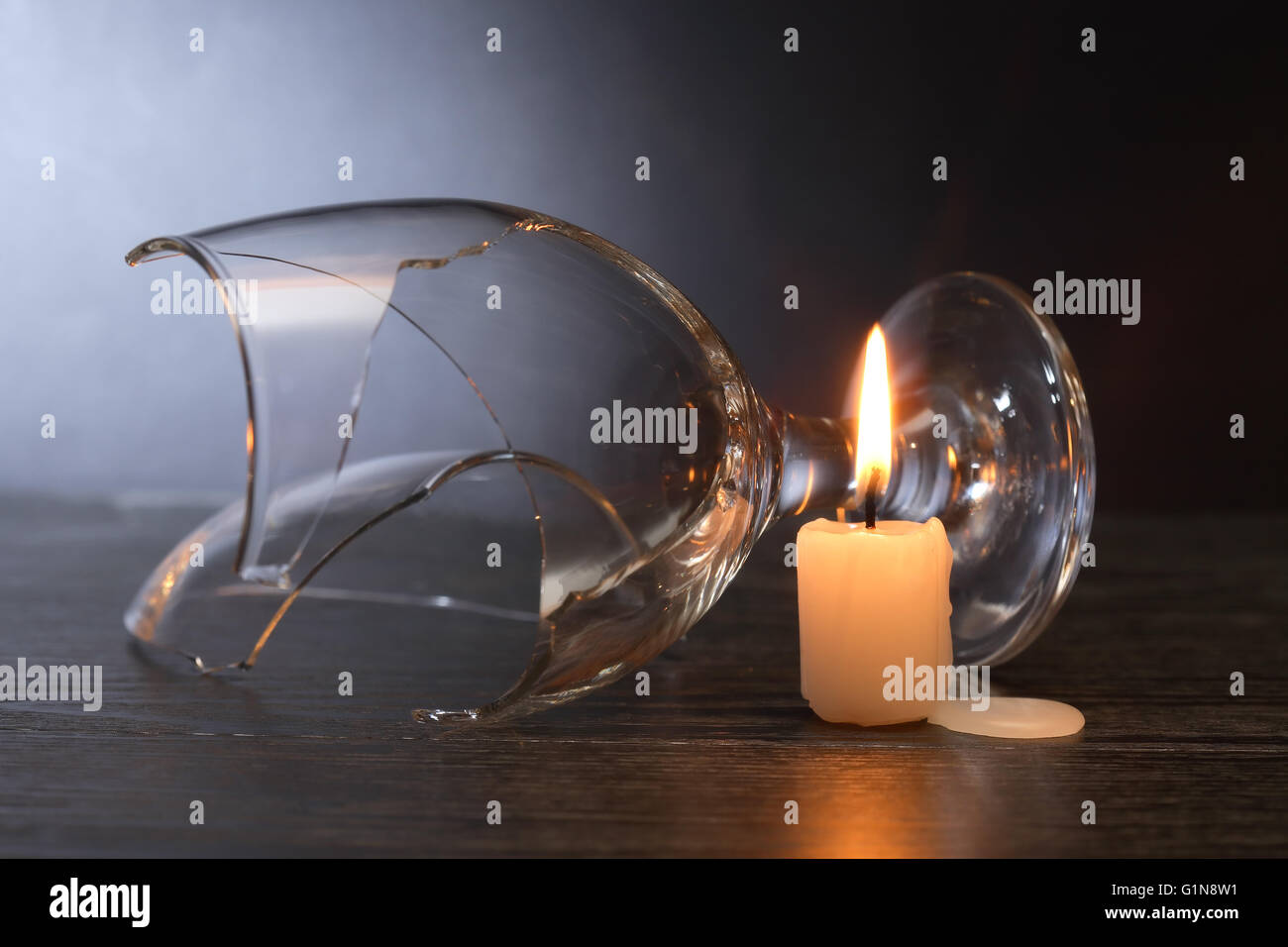 Broken wineglass near lighting candle on dark background Stock Photo