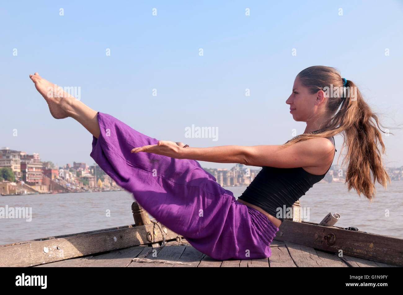 Young female practising yoga pose Navasana on the boat over Ganga river ...