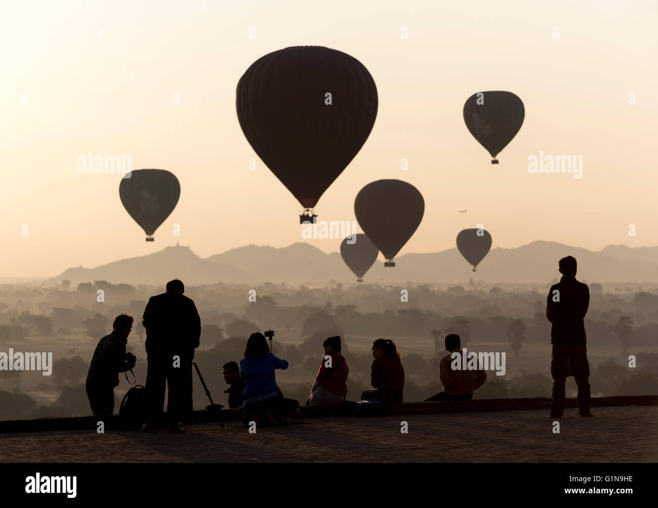 Tourists take photographs of hot-air balloons over temples of Bagan at sunrise, Pyathada Paya, Burma - Myanmar Stock Photo