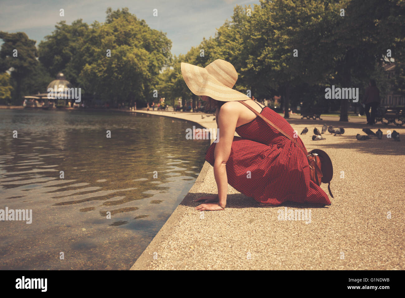 A young woman in a red dress is sitting by a lake in a park Stock Photo ...