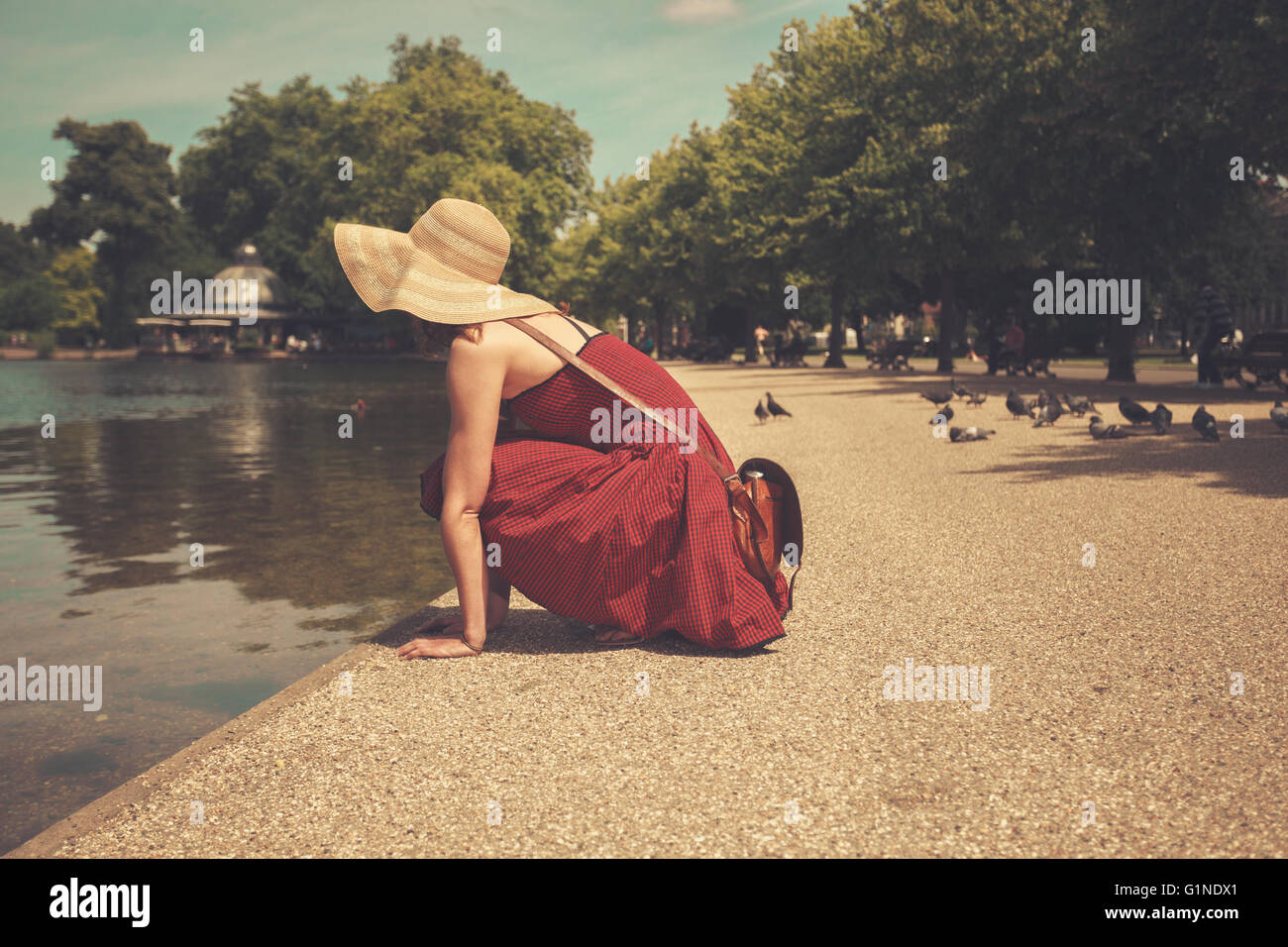 A young woman in a red dress is sitting by a lake in a park Stock Photo ...