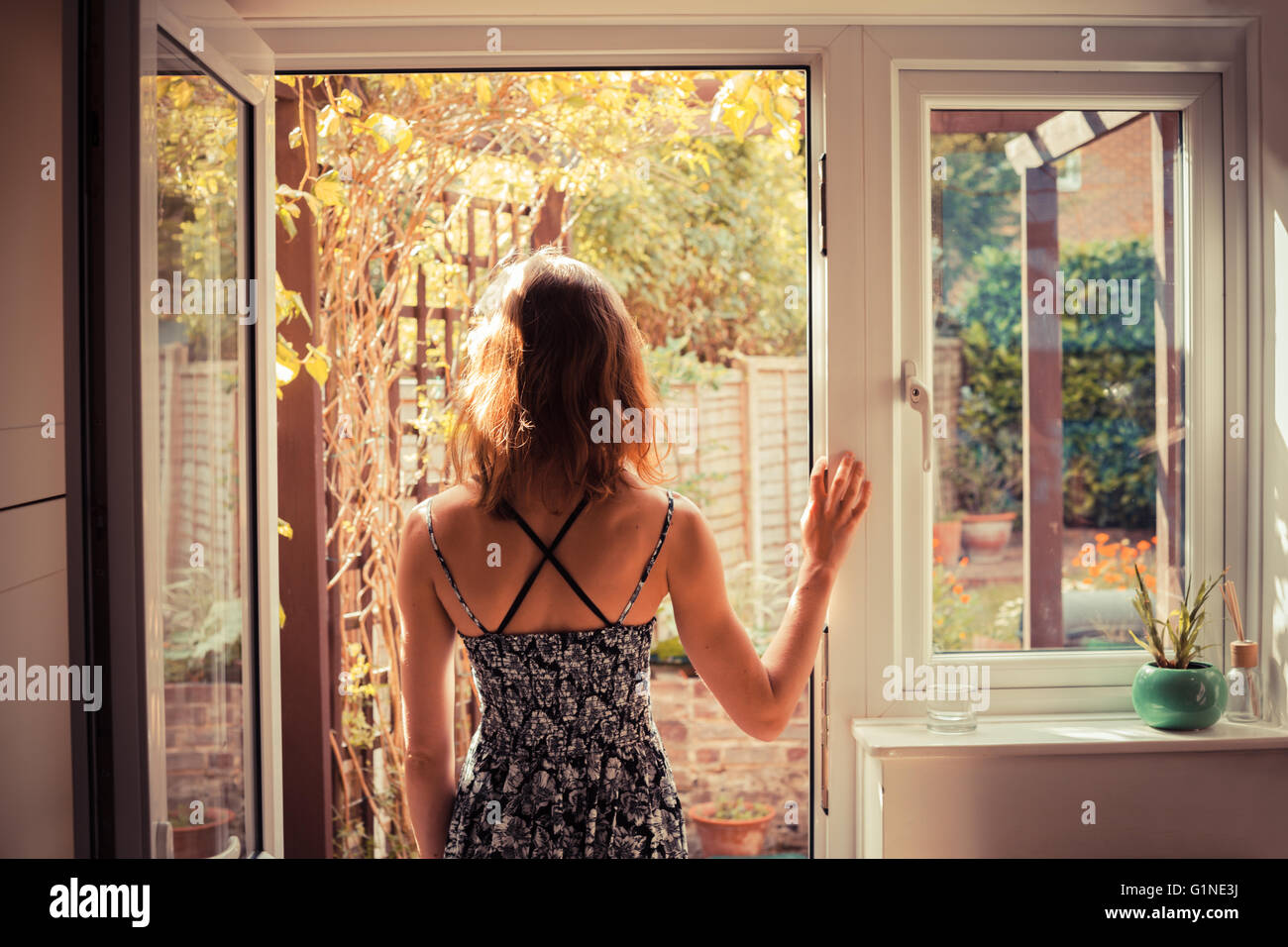 A young woman is standing in the doorway of her kitchen and is looking ...