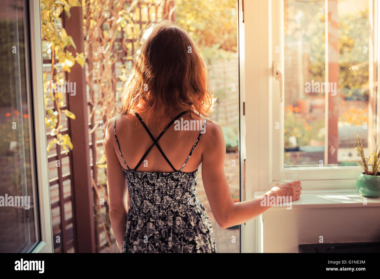 A young woman is standing in the doorway of her kitchen and is looking ...