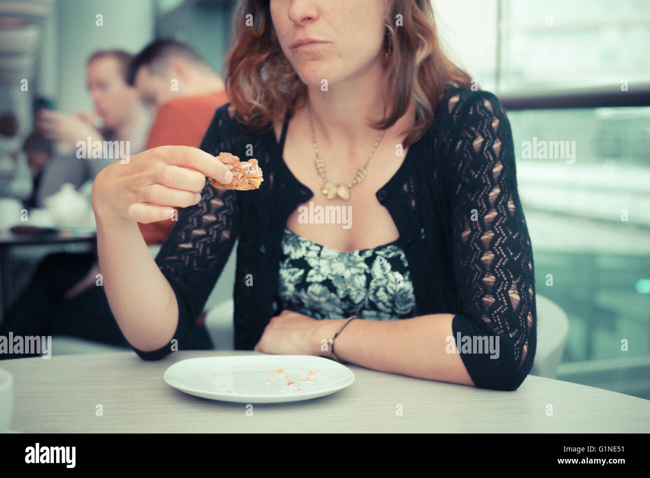 A young woman is having coffee and cake by the window in an airport Stock Photo
