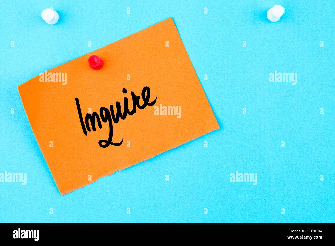 Inquire written on orange paper note pinned on cork board with white thumbtack, copy space available Stock Photo