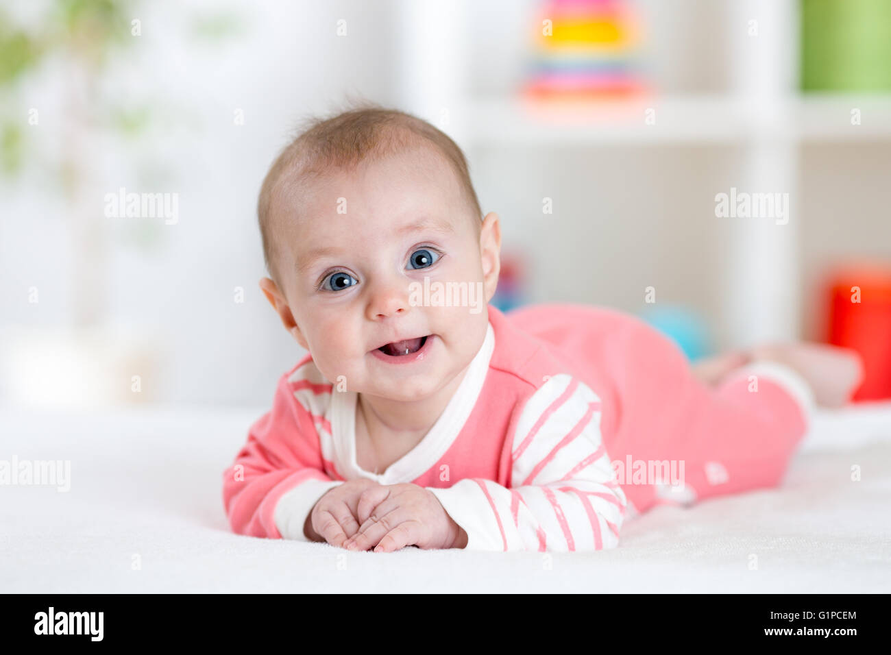 Very happy laughing baby in pink clothes lying on his belly. Infant looking straight at the camera Stock Photo