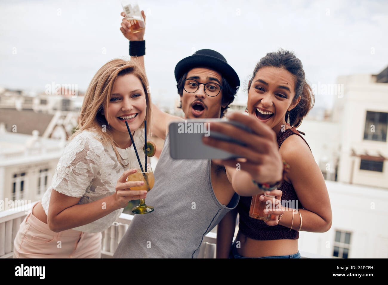 Excited young people taking self portrait with mobile phone during a party. Happy young man and woman taking self portrait at ro Stock Photo