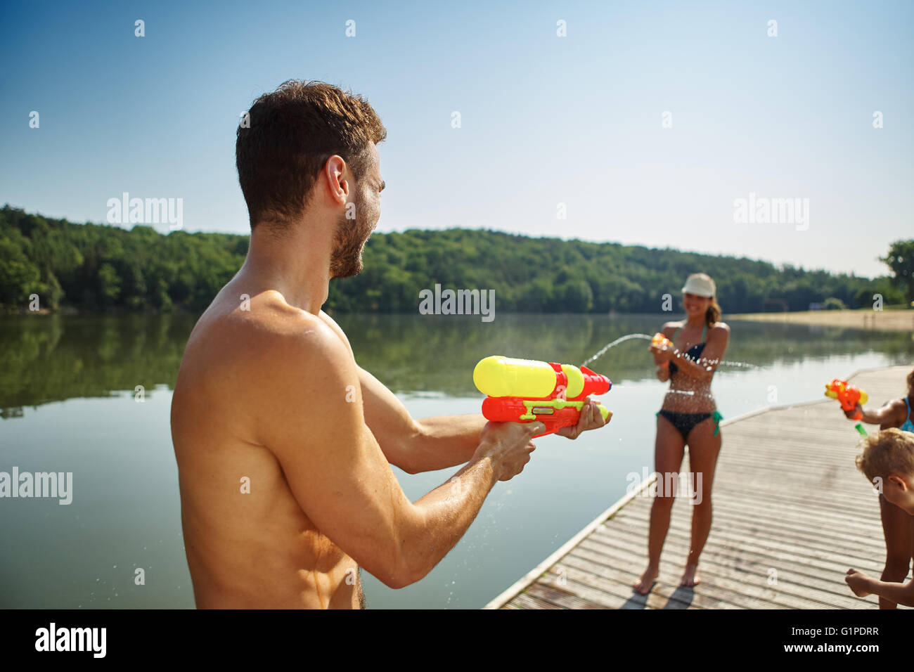 Family having fun and spraying each other with squirt guns in summer Stock Photo