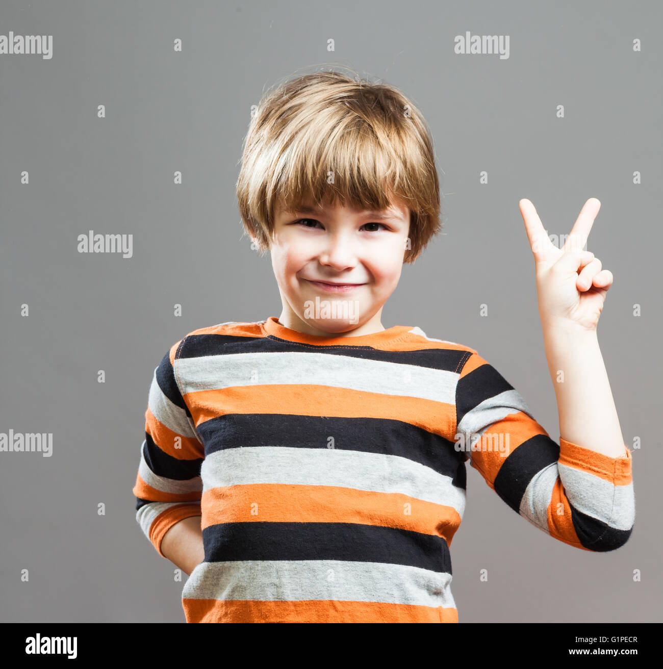 Cute Preschooler having fun in orange black striped shirt, making a Peace Sign with his Fingers Stock Photo