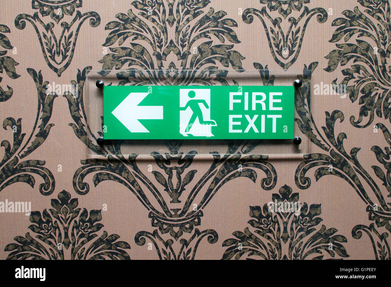Green fire exit sign on a wallpapered hotel wall Stock Photo