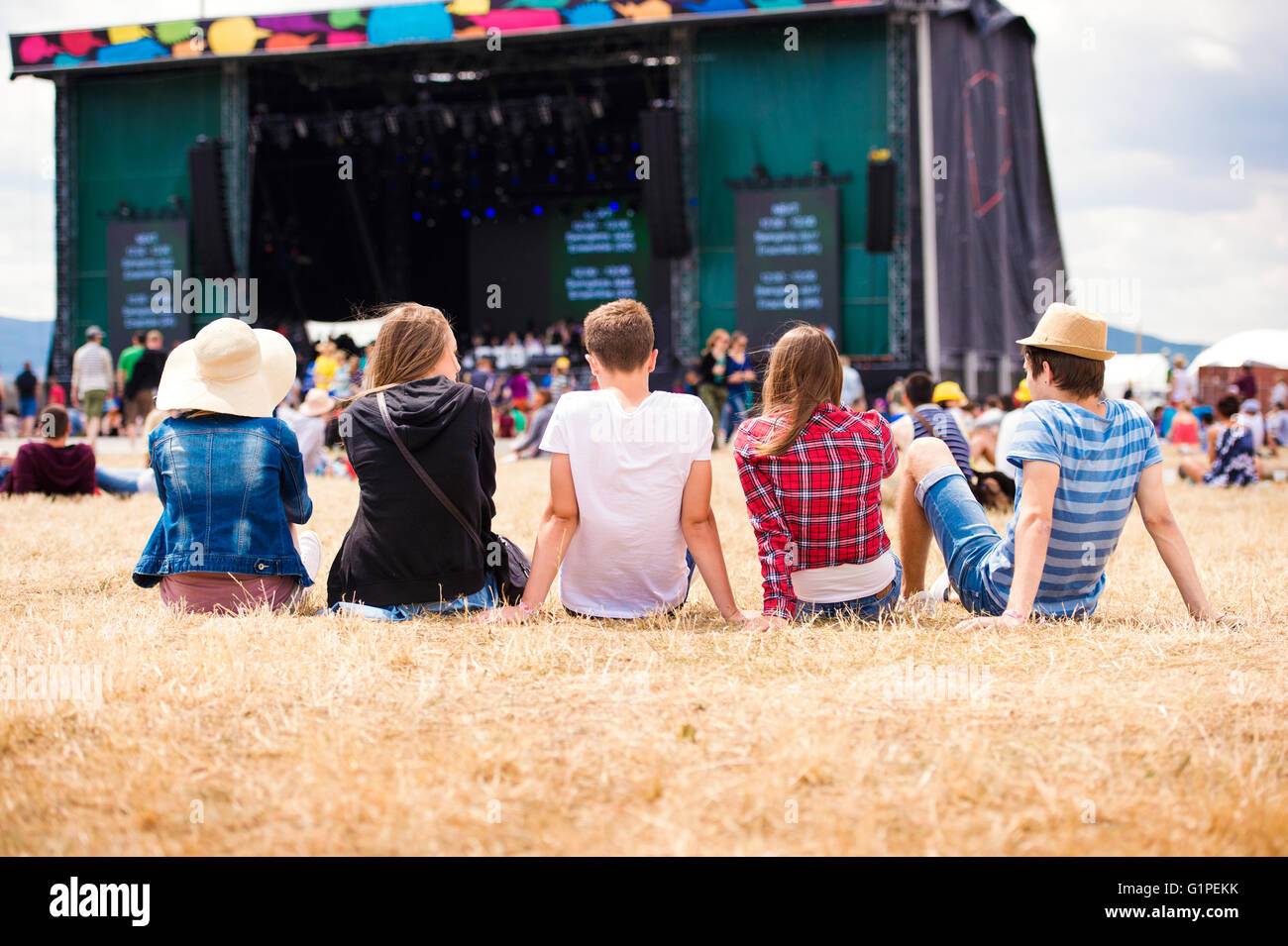 Teenagers, summer music festival, sitting in front of stage Stock Photo