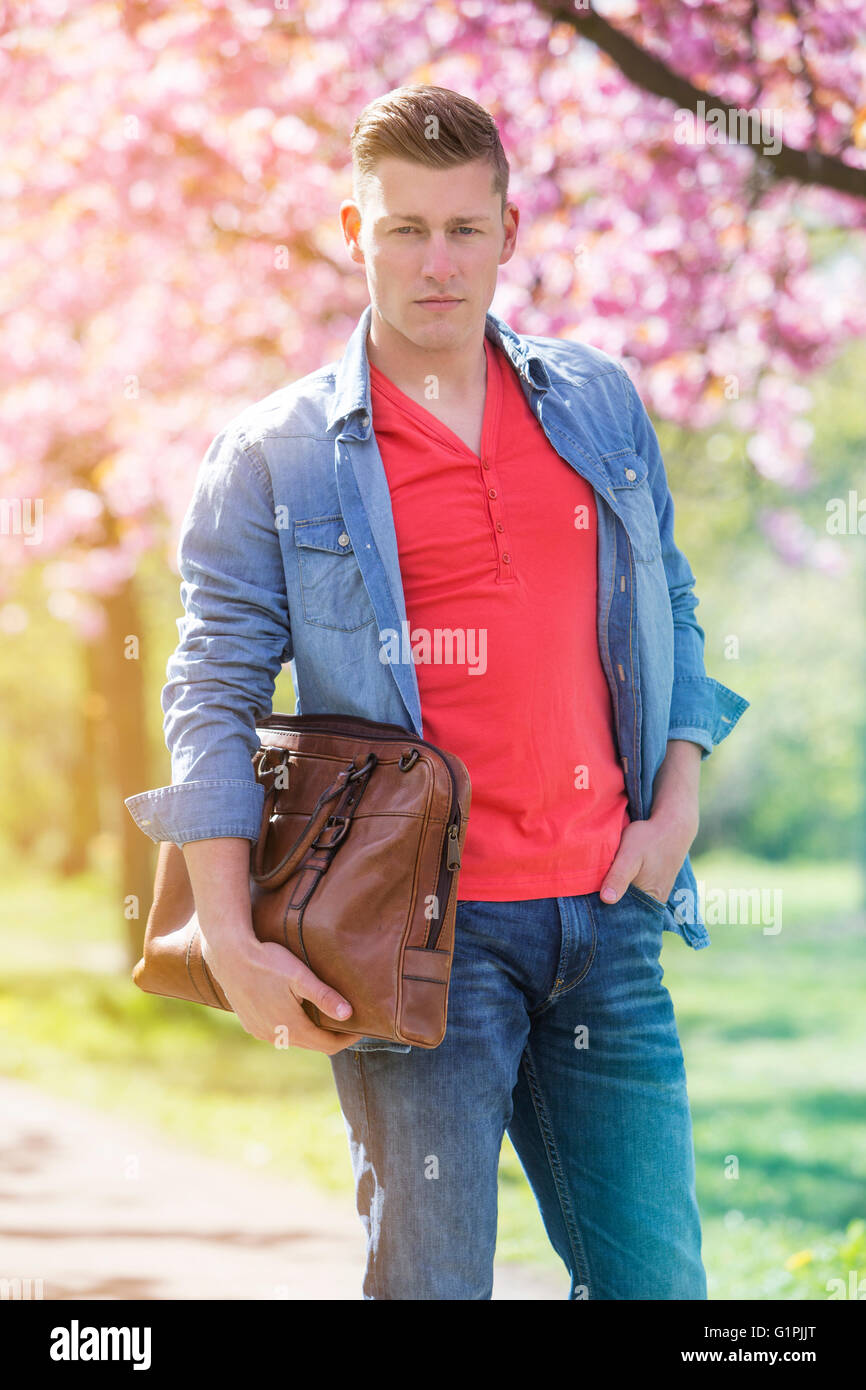 young man standing next to cherry blossom holding a bag Stock Photo - Alamy