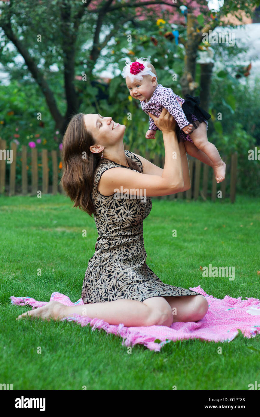 child and parenthood concept - happy mother with little baby sitting on blanket in park Stock Photo