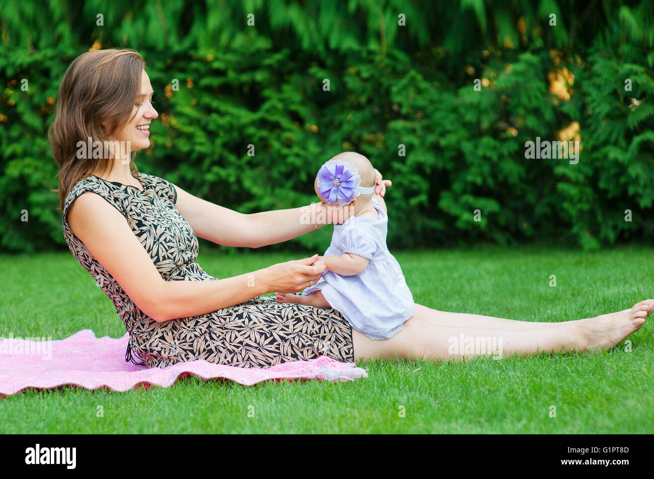 child and parenthood concept - happy mother with little baby sitting on blanket in park Stock Photo