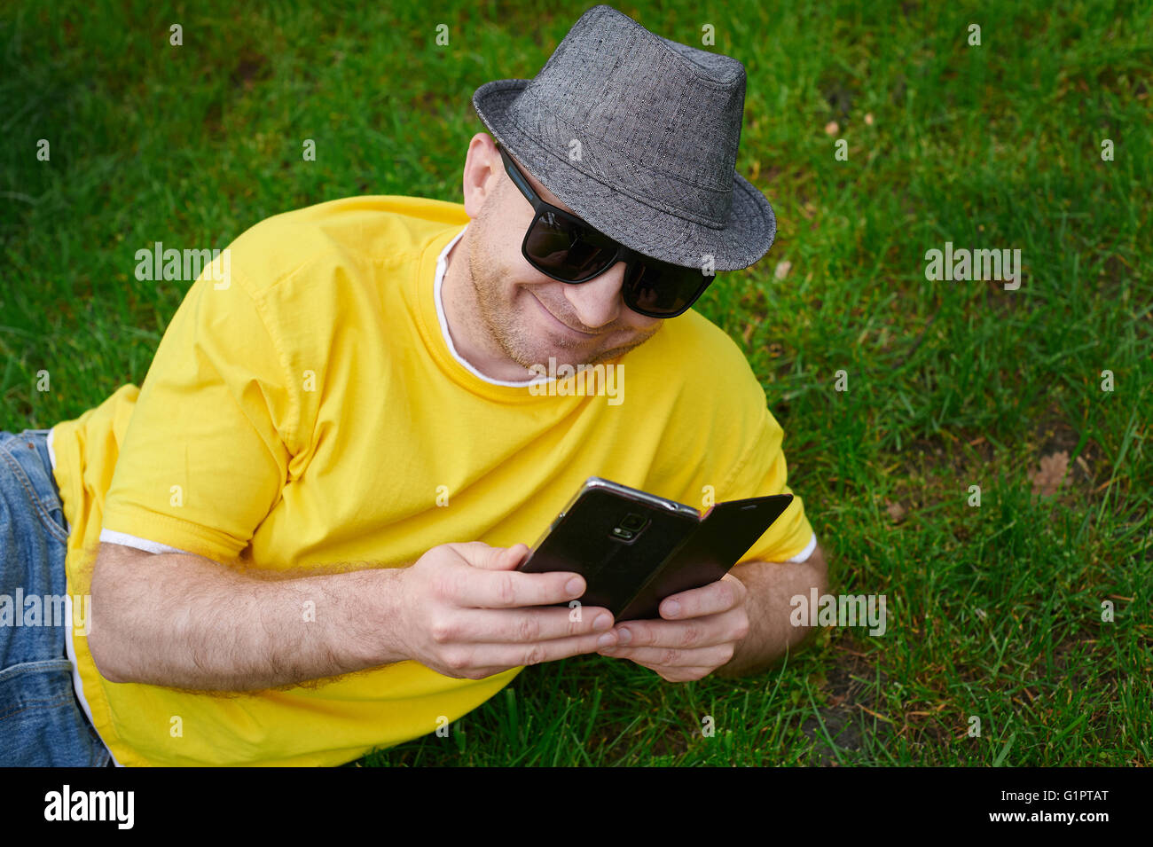 smart young man in a yellow T-shirt with the phone on the grass Stock Photo
