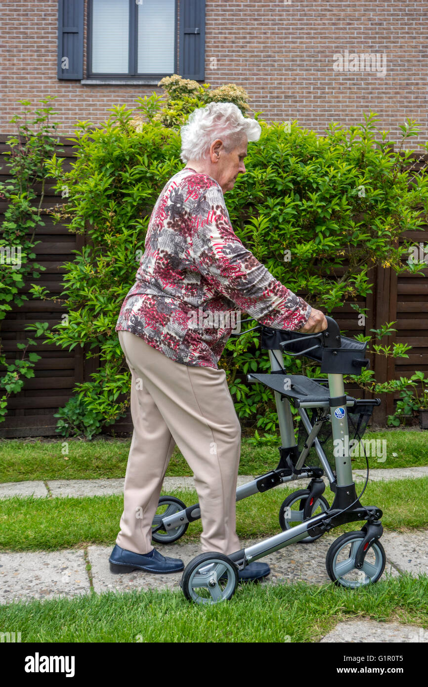 Elderly woman with rollator / wheeled walker practising walking on driveway at home Stock Photo