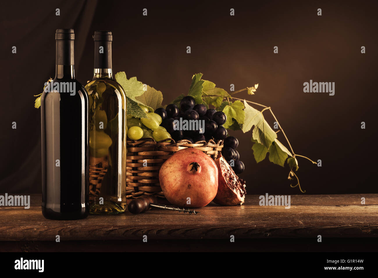 Wine bottles, corkscrew and grapes in a basket on a wooden table, wine tasting still life Stock Photo