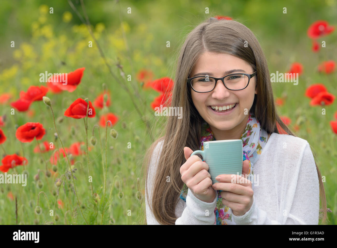 Teen girl drink cup of tea on poppy field Stock Photo
