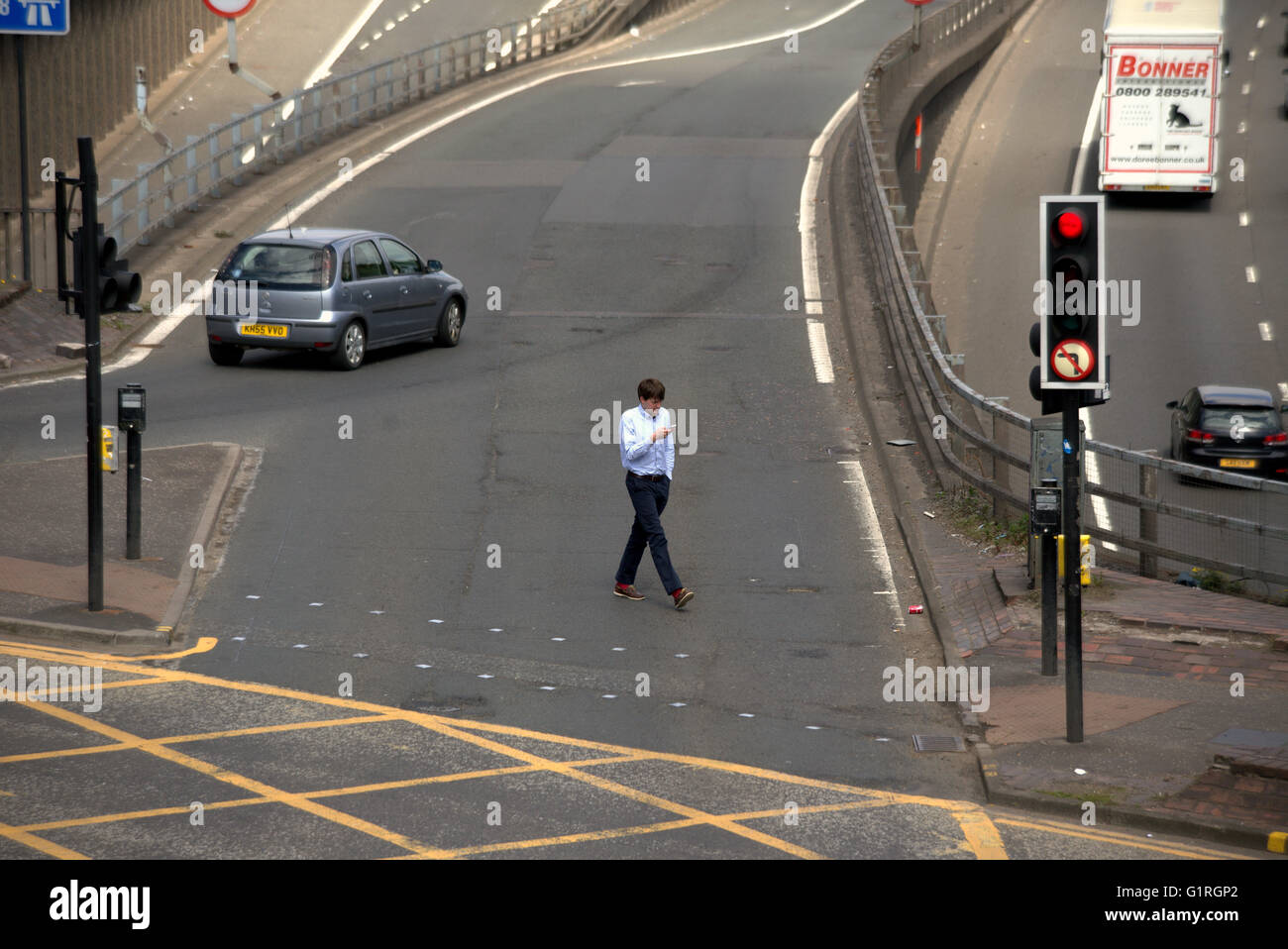 Young man crossing road whilst looking at phone at traffic lights intersection viewed from above,Glasgow, Scotland, UK Stock Photo