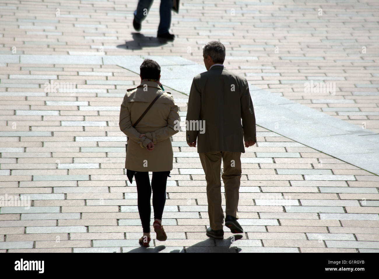 couple walking tiled street as tourists silhouetted man and woman, Glasgow, Scotland, UK. Stock Photo