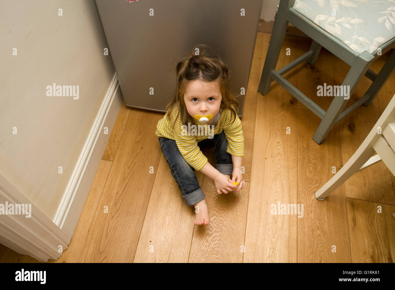 female toddler sat on floor in kitchen Stock Photo