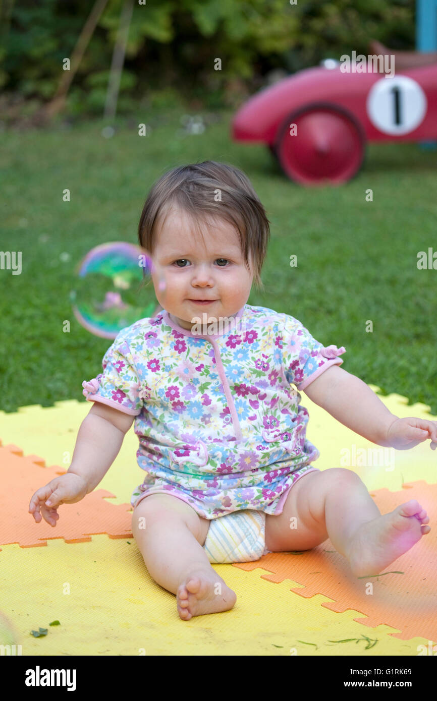 baby girl sat down watching bubble floating by in garden Stock Photo