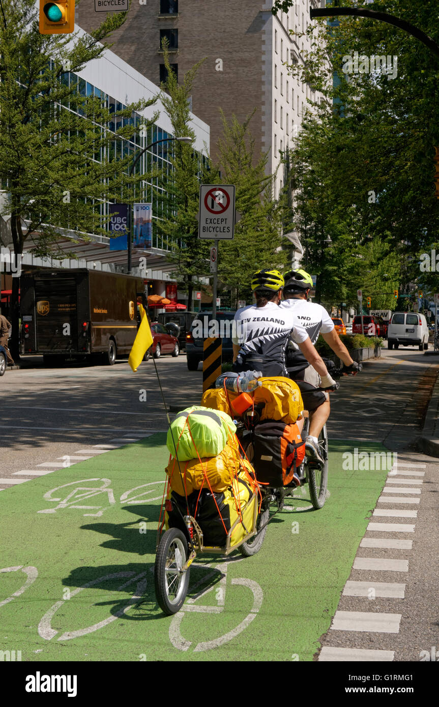 Travellers with camping gear riding tandem bicycle in downtown Vancouver, Canada Stock Photo
