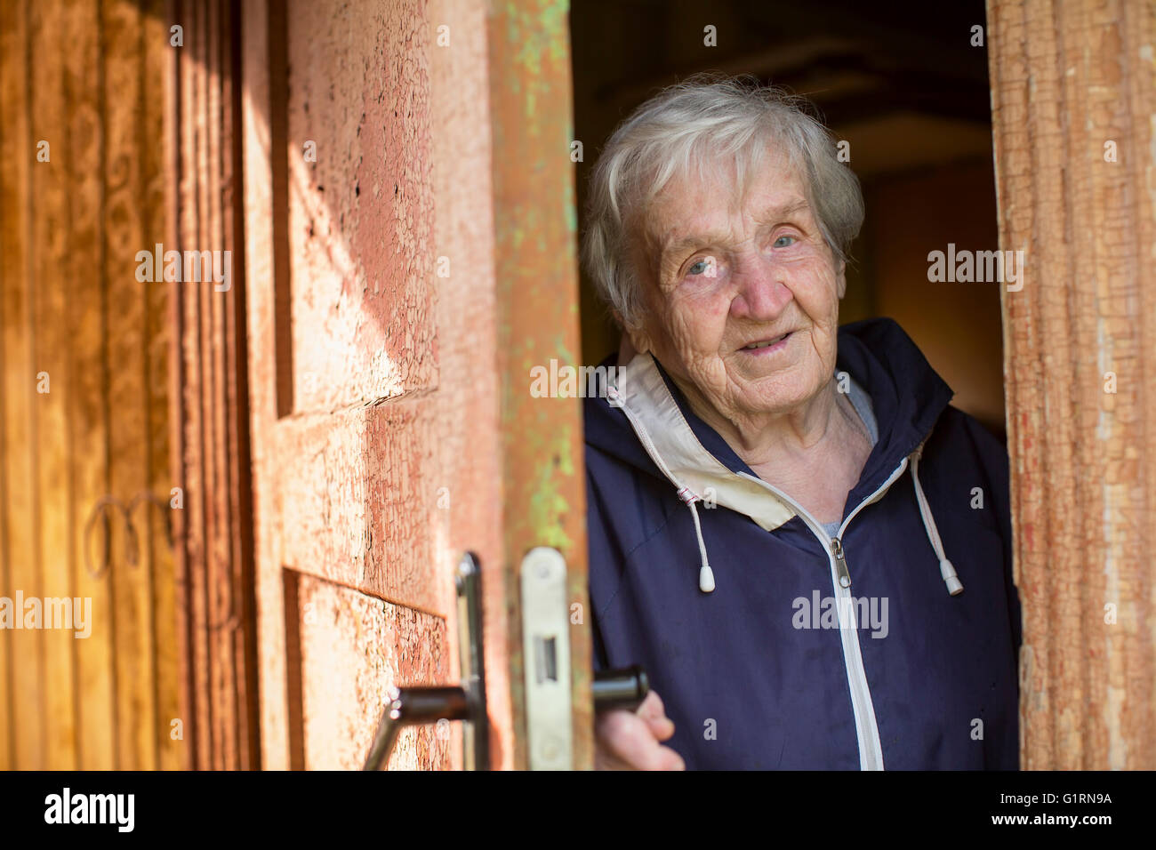 An elderly woman opens the door of the house. Stock Photo