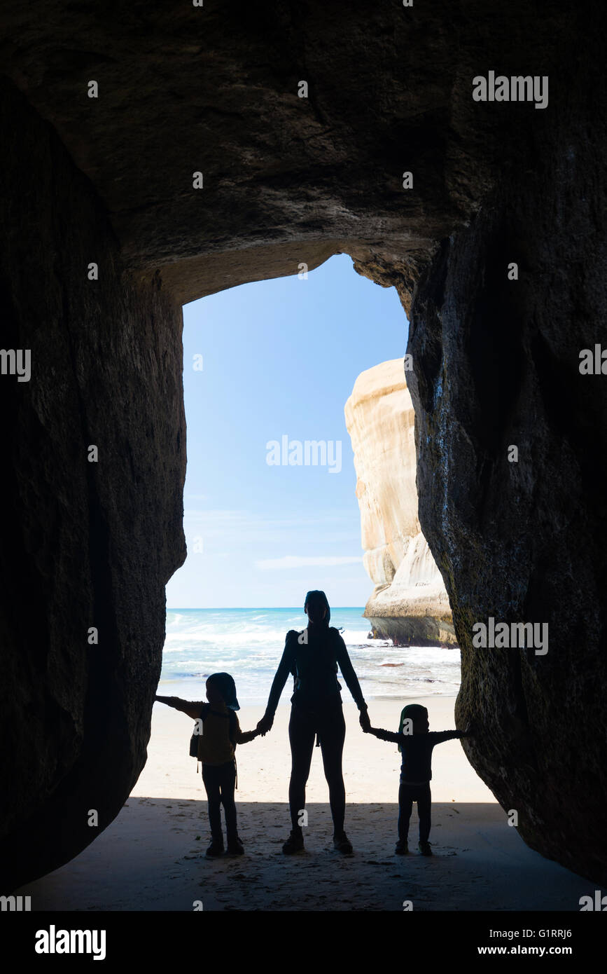 Silhouette of mother with two kids in a cave at Tunnel beach near Dunedin, New Zealand Stock Photo