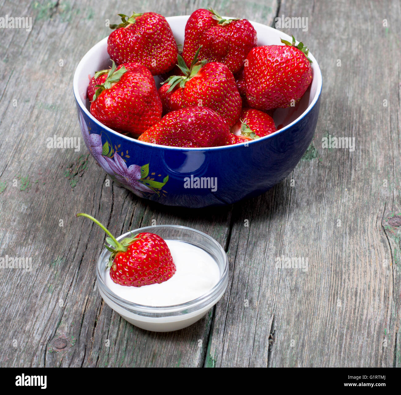 plate strawberry and one strawberry in a saucer with cream, on a wooden table Stock Photo
