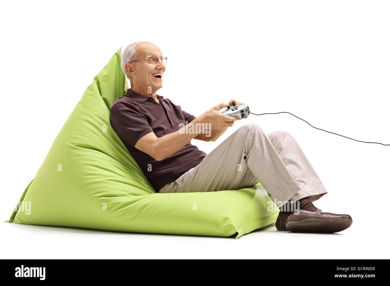 Joyful senior gentleman playing video games seated on a green beanbag isolated on white background Stock Photo