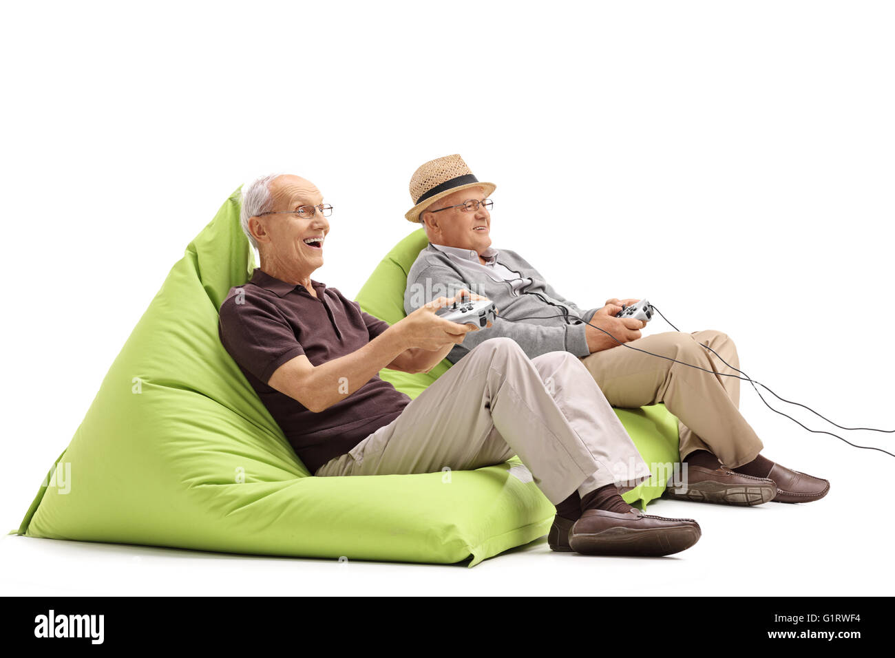 Two seniors sitting on green beanbags and playing video games isolated on white background Stock Photo