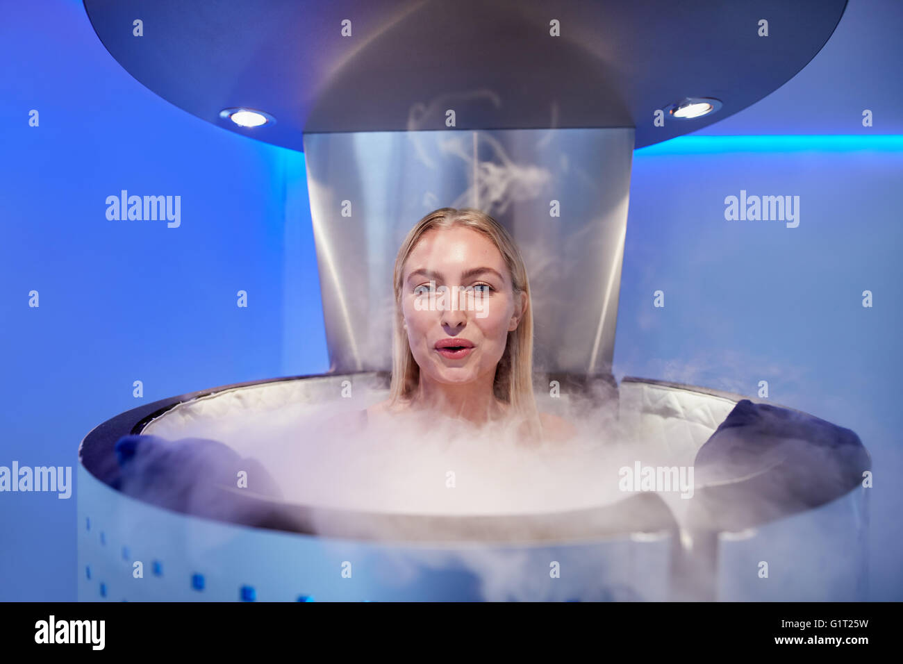 Portrait of happy young woman in a whole body cryotherapy cabin. She is looking at camera and smiling. Stock Photo
