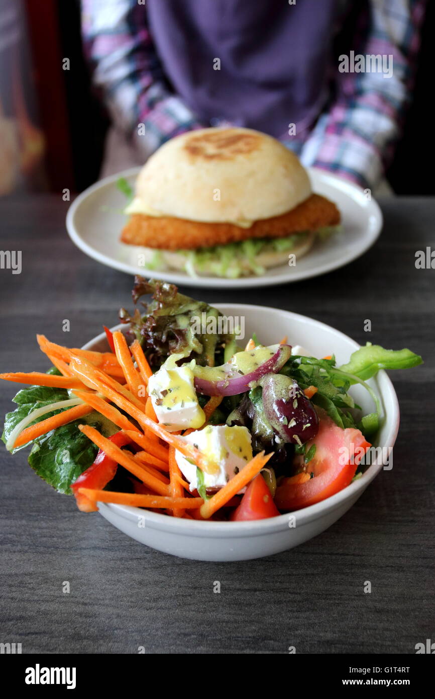 A bowl of Greek salad in a white bowl and chicken schnitzel in the background Stock Photo