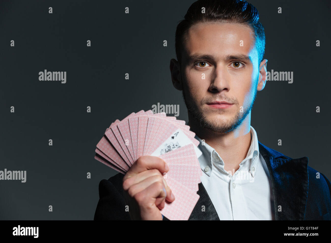 Serious young man magician holding playing cards with ace over grey background Stock Photo