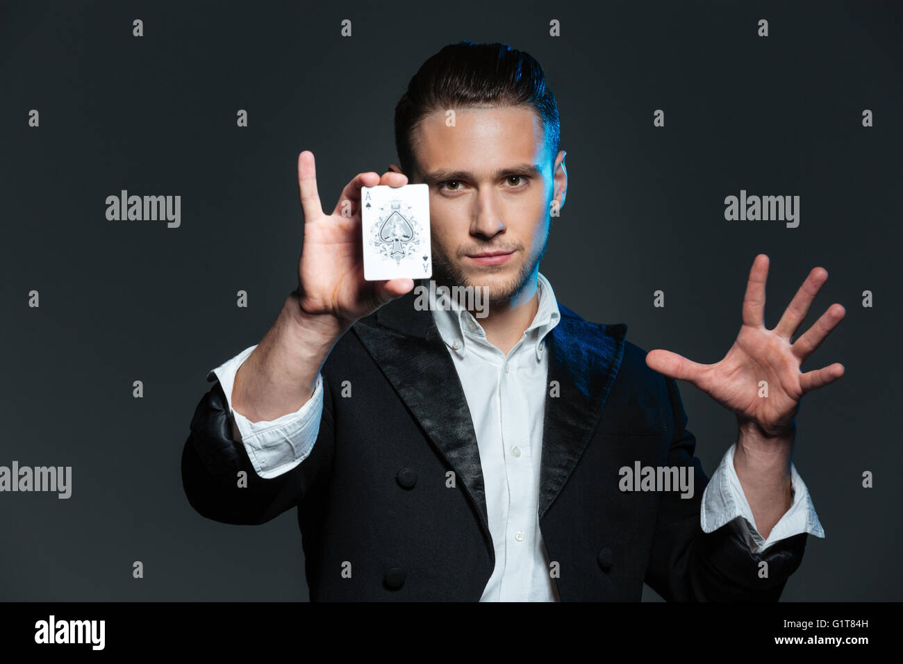 Confident young man magician showing ace card over grey background Stock Photo